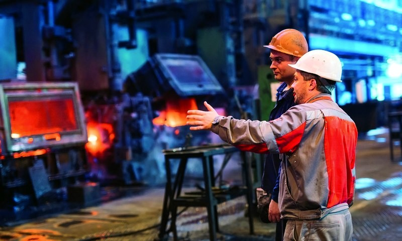 Two workers monitoring an open furnace on a plant floor